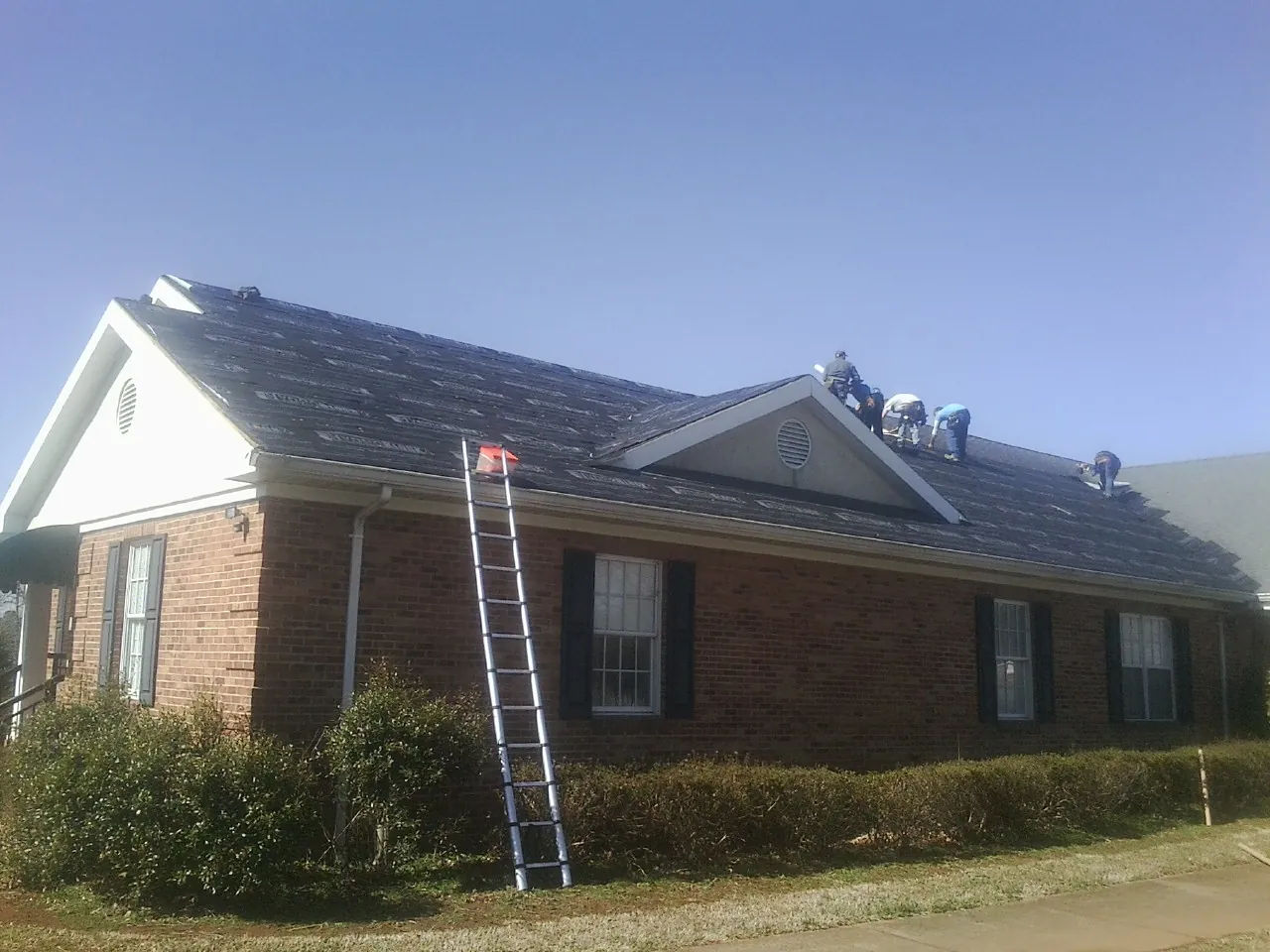 Crew tearing shingles off a brick ranch roof with a ladder set — Emergency Roof Repair work by our crew in Vermontville