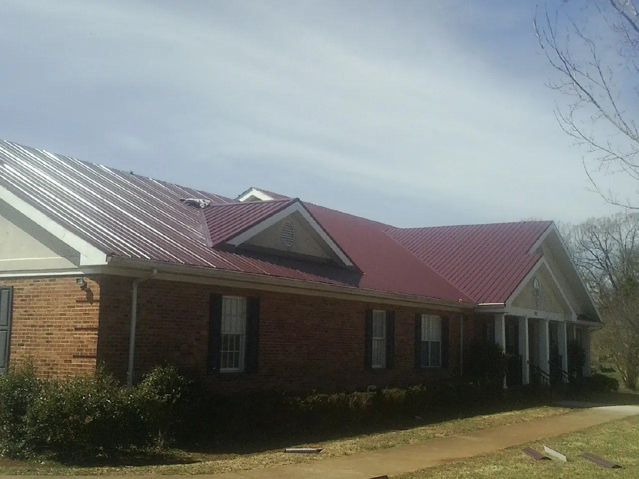 Red metal roof with gabled entries on a long brick building, from a Hail Damage Roof Repair job in Vermontville