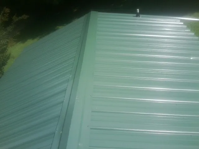 New green metal panels meeting at the ridge of a roof — Flat Roof Repair work by our crew in Vermontville