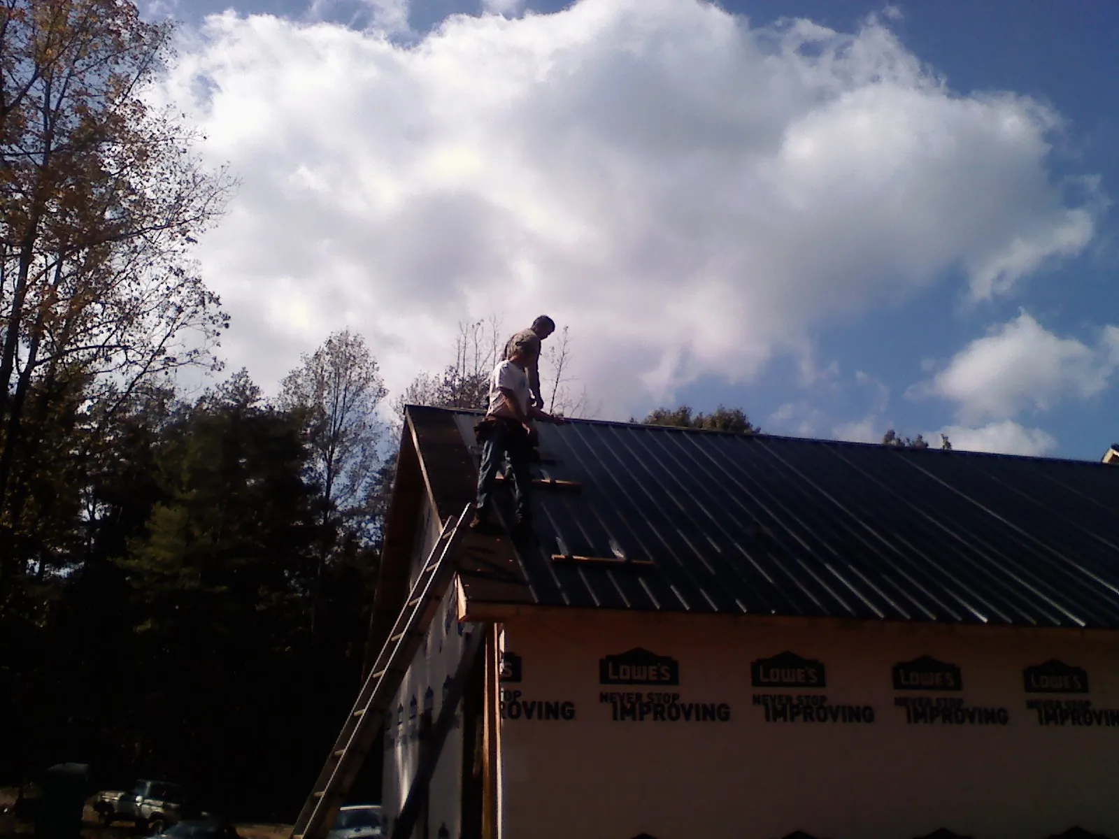 Roofer fastening dark metal panels high against a cloudy sky, from a Roof Inspection job in Vermontville