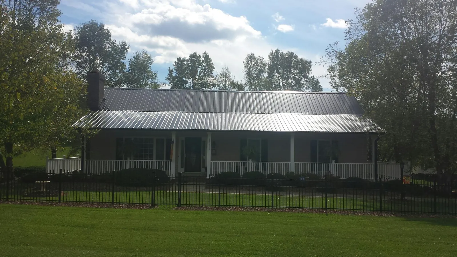 Gray metal roof on a brick ranch with a full width front porch — Gutter Guard Installation work by our crew in Vermontville