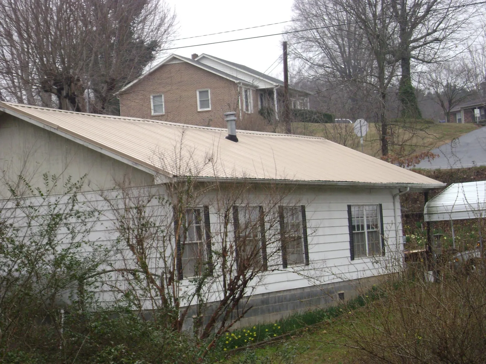 Tan metal roof on a white sided house set into a hillside — Commercial Roofing by Roofing Brothers in Vermontville